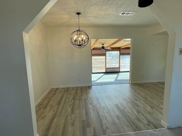 unfurnished dining area with hardwood / wood-style floors, ceiling fan with notable chandelier, and beam ceiling