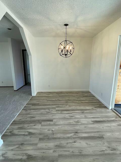 unfurnished dining area featuring a textured ceiling, light hardwood / wood-style floors, and a notable chandelier