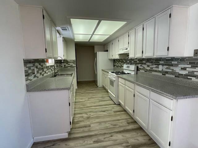 kitchen featuring backsplash, white range, sink, light hardwood / wood-style flooring, and white cabinets