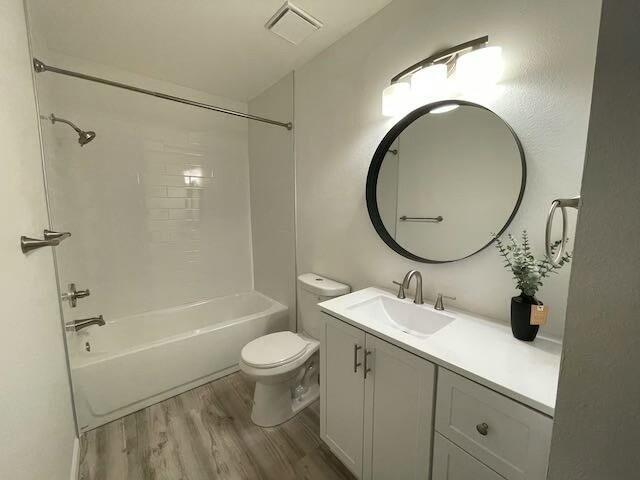 full bathroom featuring vanity, hardwood / wood-style floors, tiled shower / bath combo, and toilet