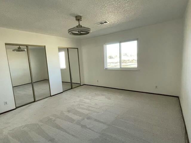 unfurnished bedroom with multiple closets, light colored carpet, and a textured ceiling