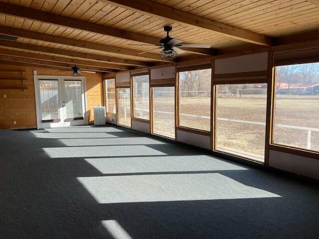 unfurnished sunroom featuring beam ceiling, ceiling fan, a healthy amount of sunlight, and wood ceiling