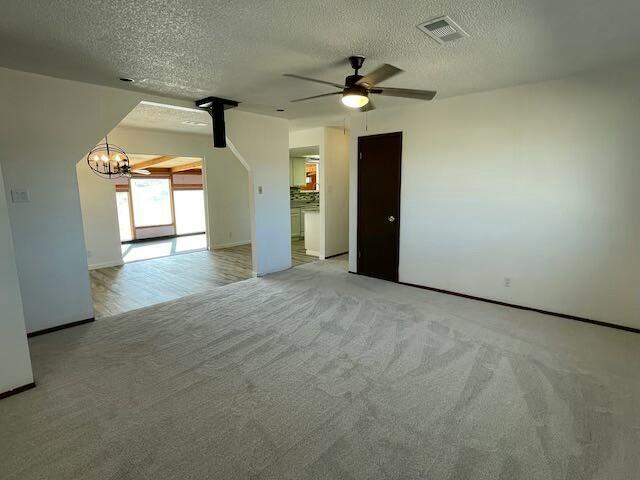 empty room with a textured ceiling, light colored carpet, and ceiling fan with notable chandelier