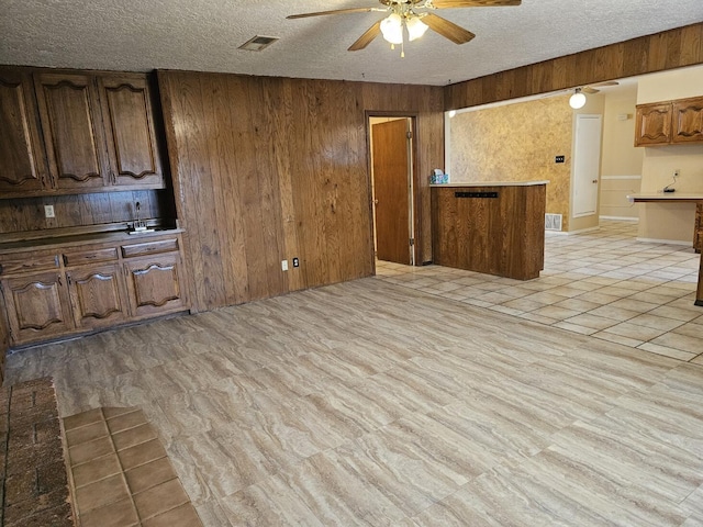 kitchen featuring ceiling fan, wooden walls, and a textured ceiling