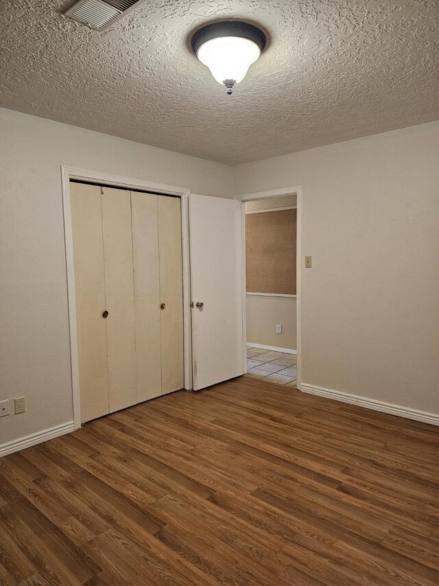 unfurnished bedroom featuring a textured ceiling, a closet, and hardwood / wood-style floors