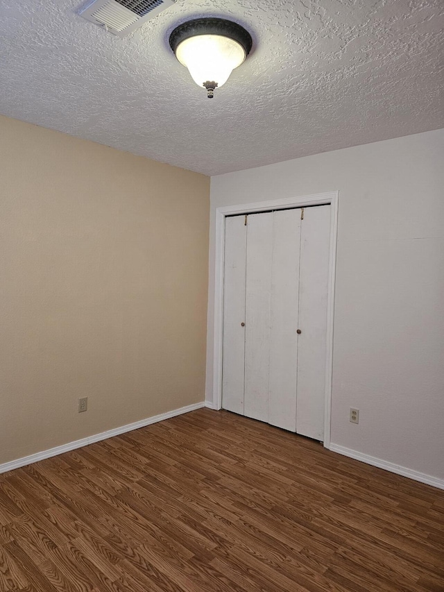 unfurnished bedroom with a textured ceiling, dark wood-type flooring, and a closet