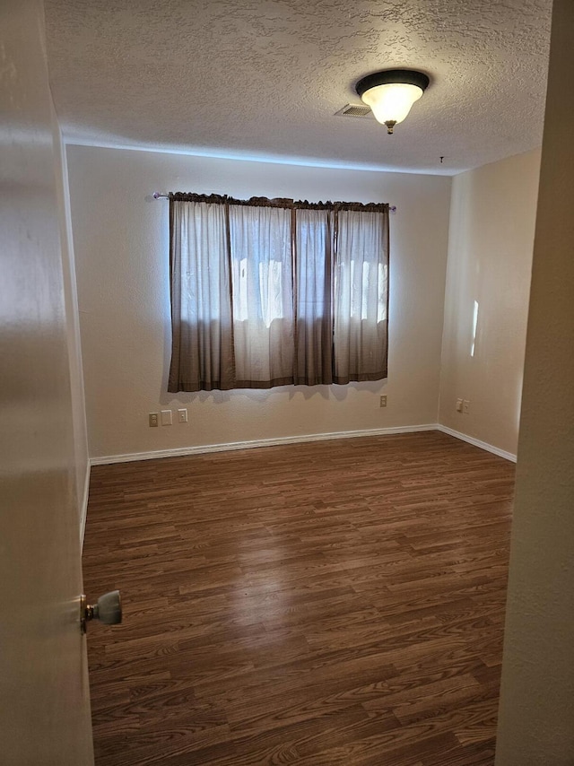 spare room with a textured ceiling and dark hardwood / wood-style flooring