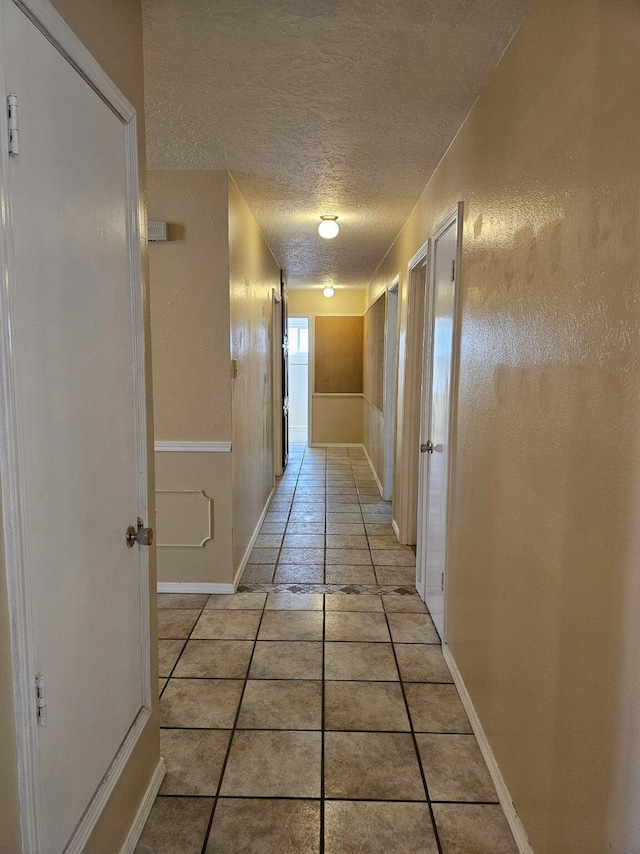 corridor featuring a textured ceiling and light tile patterned floors