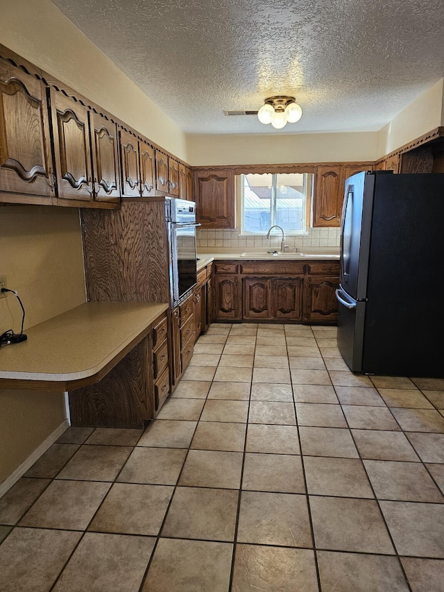 kitchen with sink, oven, light tile patterned flooring, backsplash, and stainless steel fridge