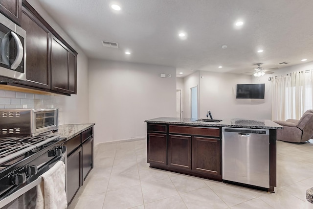 kitchen featuring light tile patterned floors, dark brown cabinetry, stainless steel appliances, and dark stone counters