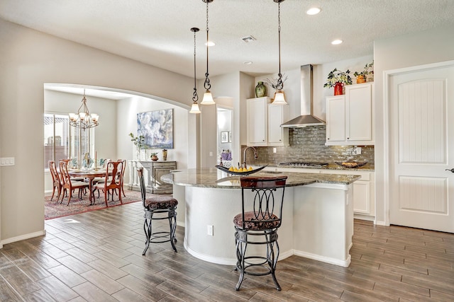 kitchen with stainless steel gas cooktop, wall chimney exhaust hood, tasteful backsplash, wood tiled floor, and a kitchen breakfast bar