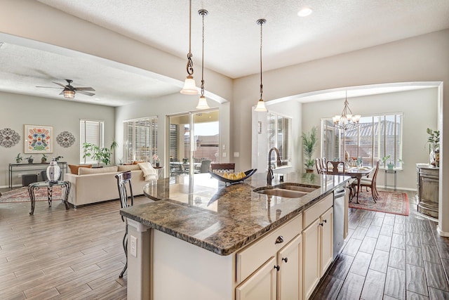 kitchen featuring a sink, open floor plan, wood tiled floor, dishwasher, and dark stone countertops