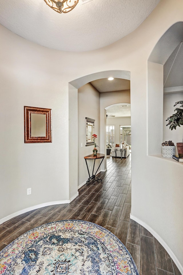 hall featuring arched walkways, wood finish floors, a textured ceiling, and baseboards