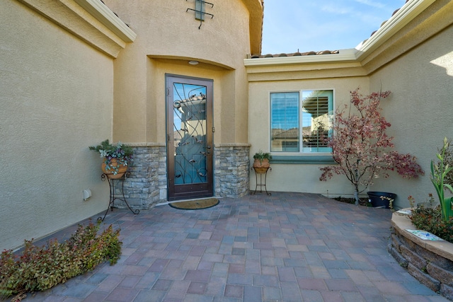 doorway to property featuring stone siding, a patio, a tiled roof, and stucco siding