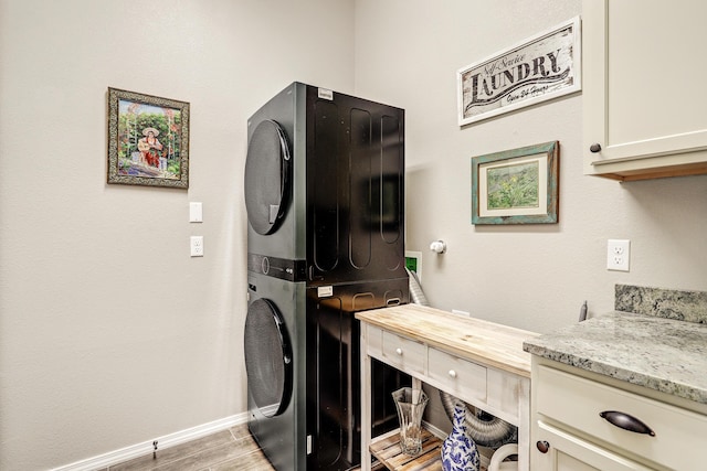 laundry area with light wood-style flooring, stacked washer / dryer, cabinet space, and baseboards