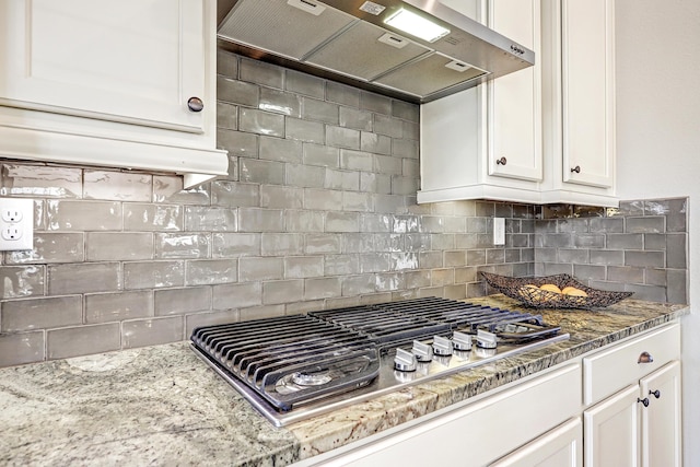 kitchen featuring white cabinets, decorative backsplash, light stone countertops, wall chimney exhaust hood, and stainless steel gas stovetop