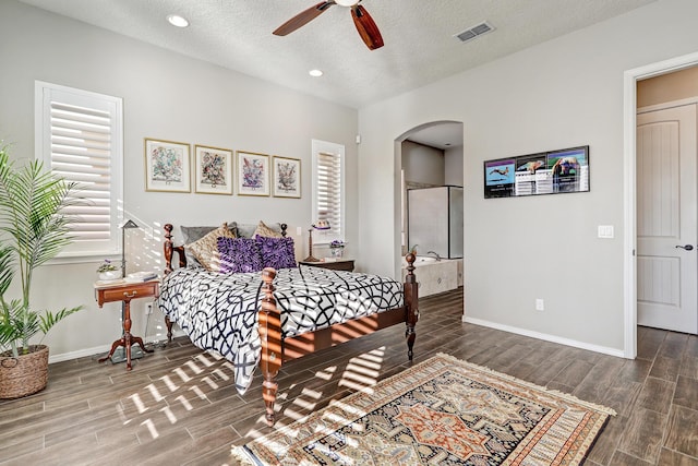 bedroom with arched walkways, a textured ceiling, wood finish floors, visible vents, and baseboards