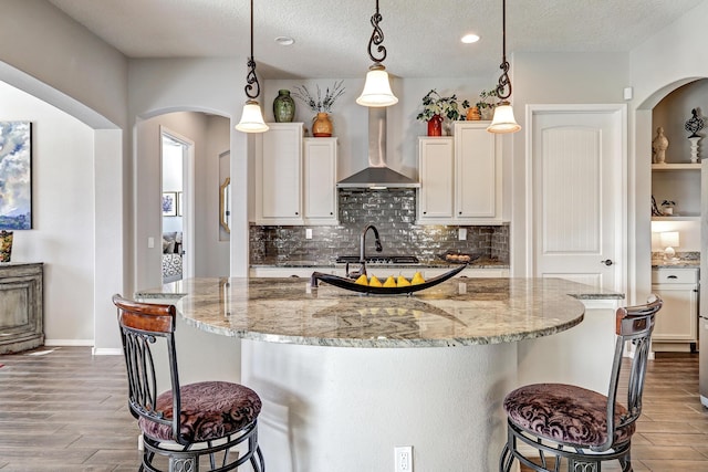 kitchen featuring wall chimney exhaust hood, a kitchen bar, arched walkways, and wood finished floors