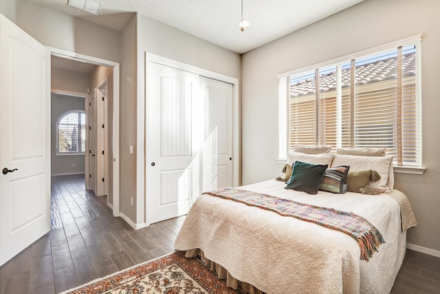 bedroom with dark wood-type flooring, a closet, and baseboards