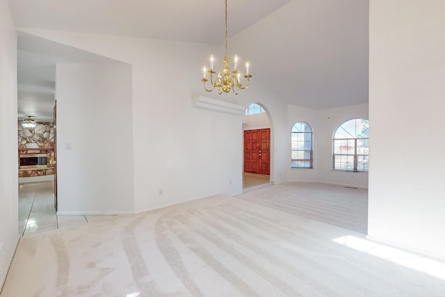 empty room with lofted ceiling, ceiling fan with notable chandelier, a fireplace, and light carpet