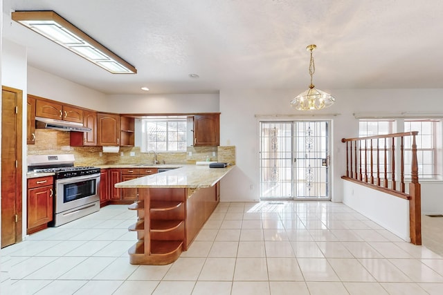 kitchen with a chandelier, kitchen peninsula, light tile patterned floors, stainless steel gas range oven, and pendant lighting