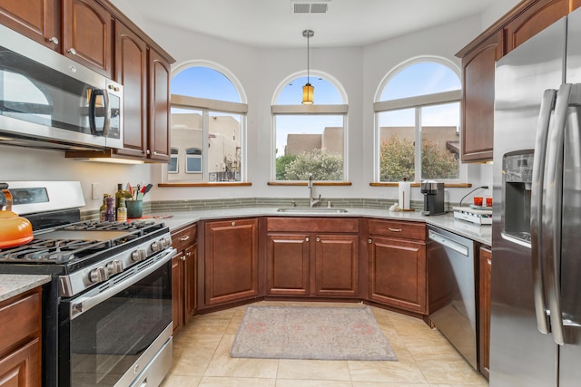 kitchen with light stone countertops, stainless steel appliances, sink, light tile patterned floors, and hanging light fixtures