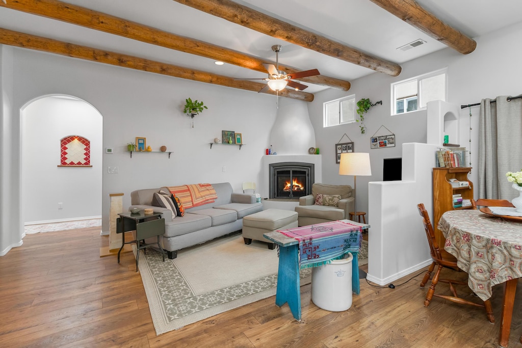 living room featuring beamed ceiling, wood-type flooring, ceiling fan, and a fireplace