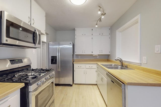 kitchen featuring light wood finished floors, a sink, stainless steel appliances, track lighting, and white cabinets