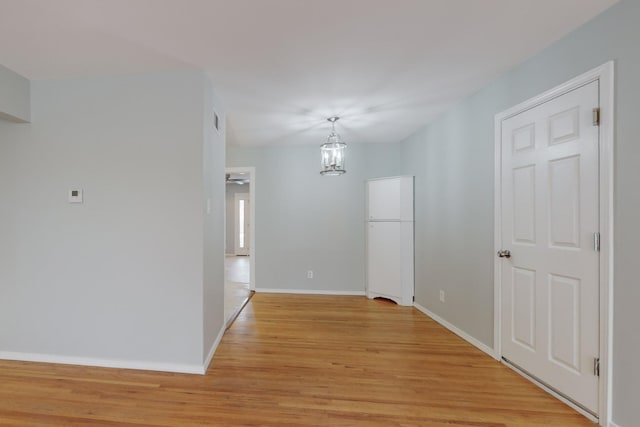 unfurnished dining area with a notable chandelier, light wood-style floors, and baseboards