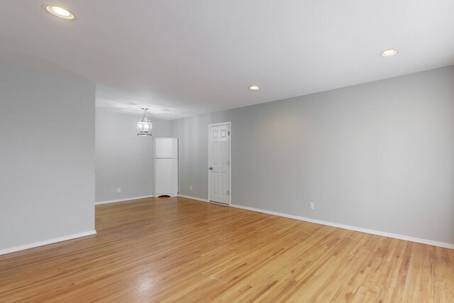 empty room featuring recessed lighting, light wood-style flooring, an inviting chandelier, and baseboards