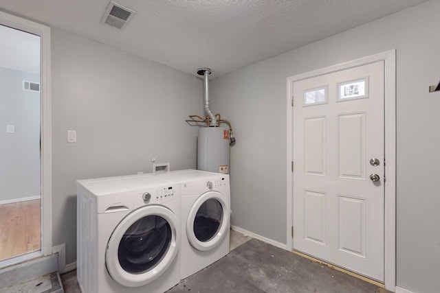 washroom featuring water heater, visible vents, washing machine and dryer, and laundry area