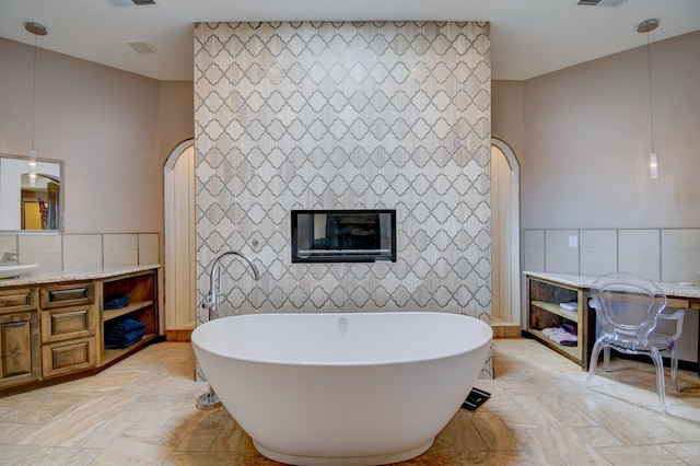 full bathroom featuring a freestanding bath, visible vents, vanity, and tile walls