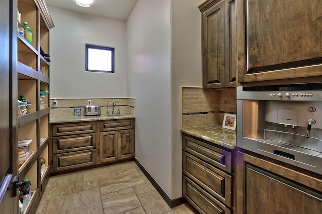 interior space featuring decorative backsplash, light stone counters, sink, and dark brown cabinets