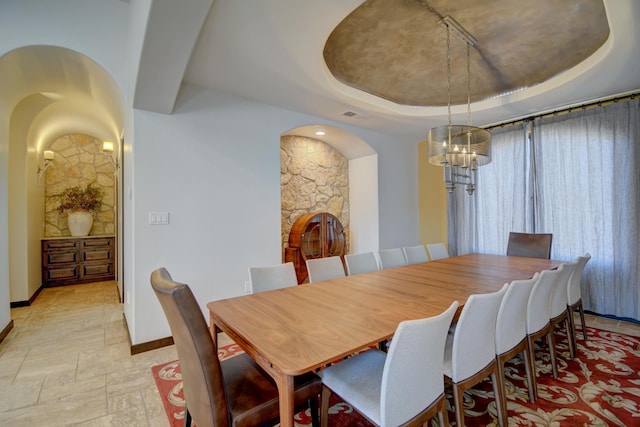 dining room featuring baseboards, a raised ceiling, and stone tile flooring