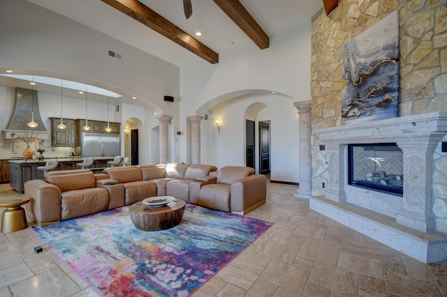 living area with stone tile flooring, a fireplace, a high ceiling, and decorative columns