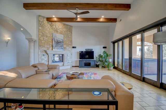 living room featuring decorative columns, stone tile floors, arched walkways, beamed ceiling, and a fireplace