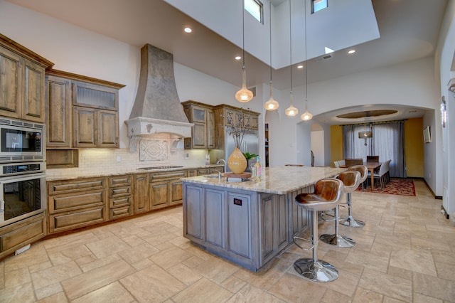 kitchen featuring arched walkways, stainless steel appliances, a spacious island, custom exhaust hood, and decorative light fixtures