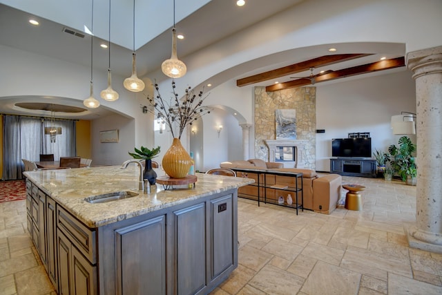 kitchen with arched walkways, a sink, hanging light fixtures, a center island with sink, and ornate columns