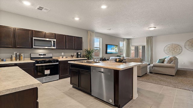 kitchen featuring sink, dark brown cabinets, stainless steel appliances, an island with sink, and light colored carpet