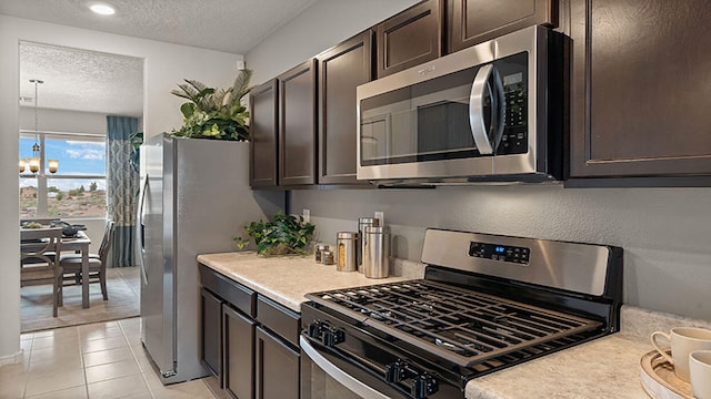 kitchen with an inviting chandelier, dark brown cabinets, light tile patterned floors, a textured ceiling, and stainless steel appliances