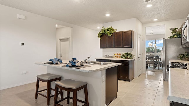 kitchen with an island with sink, sink, a kitchen bar, dark brown cabinets, and a textured ceiling