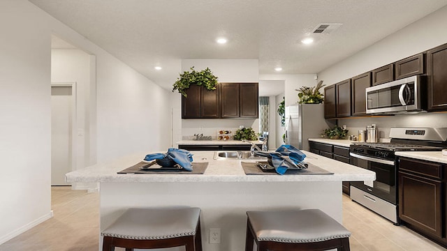 kitchen with stainless steel appliances, a kitchen breakfast bar, and an island with sink