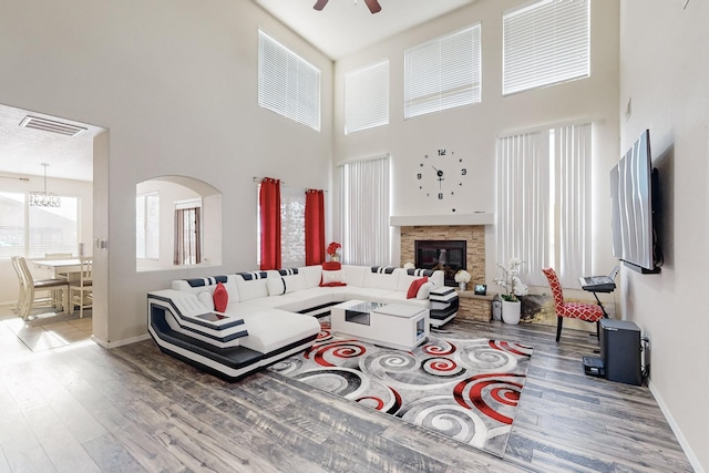 living room featuring ceiling fan with notable chandelier, wood-type flooring, a fireplace, and a high ceiling