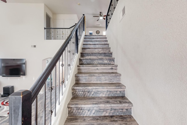 stairs with a towering ceiling, hardwood / wood-style flooring, and ceiling fan