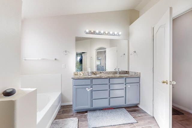 bathroom featuring a tub, vanity, and lofted ceiling