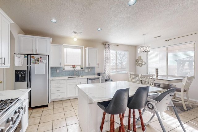 kitchen featuring hanging light fixtures, light tile patterned floors, a kitchen island, white cabinetry, and stainless steel appliances