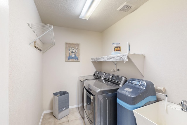 clothes washing area featuring sink, light tile patterned floors, a textured ceiling, and independent washer and dryer