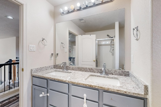 bathroom with a textured ceiling, vanity, and a shower with shower door