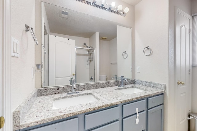 bathroom featuring a textured ceiling, vanity, toilet, and a shower with door