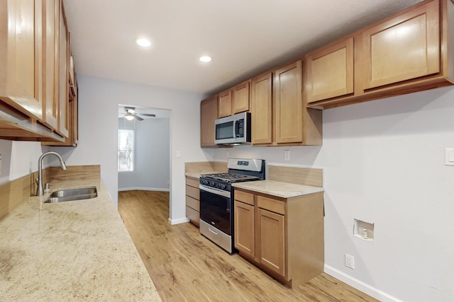 kitchen featuring light stone counters, stainless steel appliances, ceiling fan, sink, and light hardwood / wood-style flooring